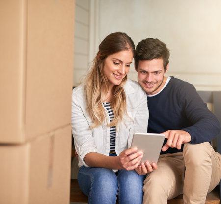 Posting their moving-day selfies on social media. a happy young couple taking a break with their tablet while moving into their new home.の写真素材