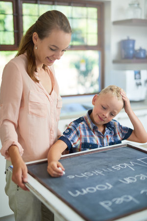 Lets see what needs to be done today. a mother and son writing chores on a chalkboard.の写真素材