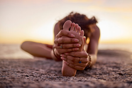 Stretching, peace and feet of a woman on beach for yoga, training and exercise during sunset. Fitness, sand and legs of girl doing warm up before workout or pilates for wellness and relax by the seaの写真素材