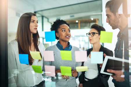It all starts with an idea. coworkers using sticky notes on a glass wall during a meeting.の写真素材
