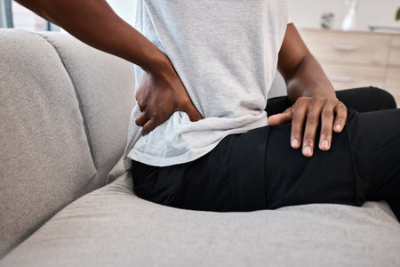 hand, back pain and woman at home on the couch after injury or accident with a bad muscle. Bruise,...