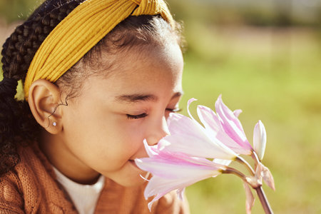 Nature, beauty and child smell flower in park, enjoying weekend, holiday and vacation in countryside. Peaceful, freedom and young black girl smelling aroma or scent of plant on field in spring timeの写真素材