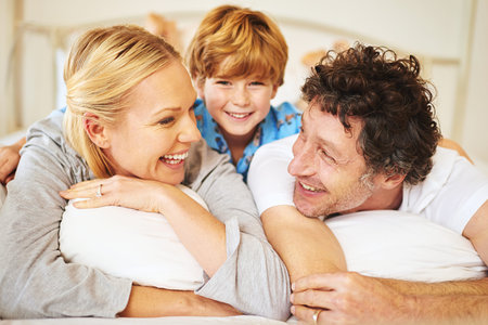 Hes always close to Mom and Dad. Portrait of a young boy lying down on a bed with his parents at...
