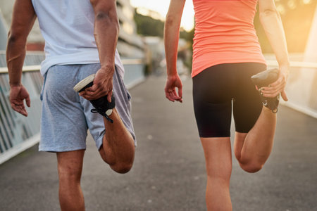 Stretching to avoid injury. Rearview shot of a young couple warming up on a bridge before their...