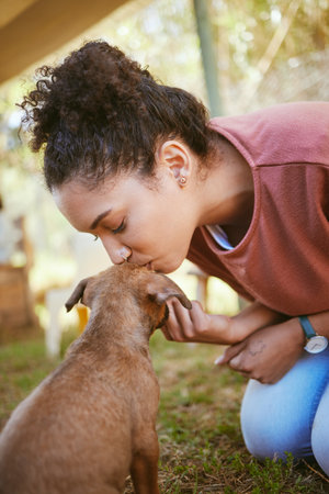 Kiss, dog and adoption with a black woman at a rescue shelter looking for a foster animal to love or care for. Kissing, love and pet with a young female adopting a puppy from a shelter to rehomeの写真素材