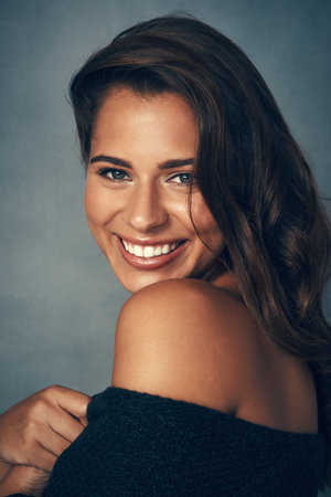 Lighting up the room with her smile. Portrait of a beautiful young woman smiling against a gray background in studio.の写真素材