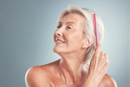 Hair, beauty and senior woman brushing hair, grooming and in studio for wellness, routine and self care on grey background. Grey hair, elderly model and comb by lady styling, relax and hygiene careの写真素材