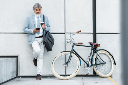 Businessman, phone and coffee with bicycle in city on social media, web or internet browsing. Tech, bike or senior manager drinking tea while on 5g smartphone app, networking or text message on breakの写真素材