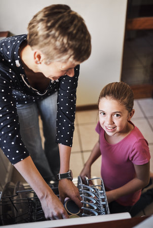 Packing the dishwasher with mom. Portrait of a cheerful mother and daughter washing dishes together at home.の写真素材