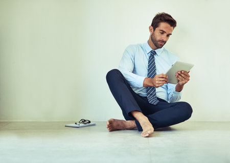 Keeping track of meetings. a young corporate businessman sitting on the ground with a digital tablet.の写真素材