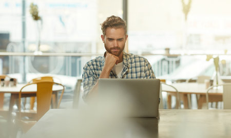 He enjoys working outside of the office. a young man using a laptop in a cafe.の写真素材