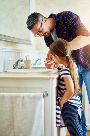 Lets get some toothpaste on that toothbrush. a handsome mature man and his daughter brushing their teeth in the bathroom.の写真素材