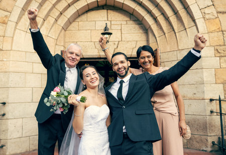 Wedding, mother and father with a happy couple in celebration of a love marriage event with family pride. Proud mom and dad smiling with a bride and groom with hands raised for a successful unionの写真素材