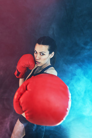 Strong never takes it easy. a young woman wearing boxing gloves against a dark background.の写真素材