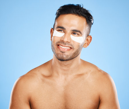 Skincare, eyes patch and man beauty, dermatology and body cosmetics of wellness, facial treatment or collagen eye care mask on studio blue background. Happy arab guy use healthy face for dark circlesの写真素材