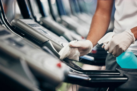 Cleaning, treadmill and sanitizing equipment in gym for bacteria, germs or protection from covid. Disinfection, sanitizer and closeup of cleaner wiping running machine for fitness in sports center.の写真素材