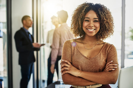 Theres nowhere else Id rather work. Portrait of a businesswoman standing with her arms folded while some colleagues talk in the background.の写真素材