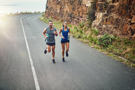 Enjoying the long road by running on it. a young attractive couple training for a marathon outdoors.の写真素材
