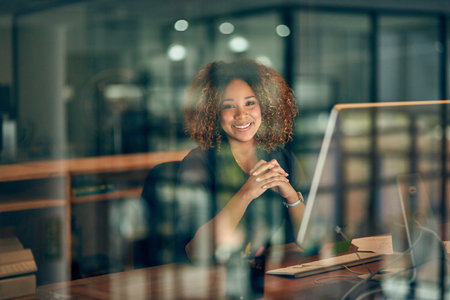 Clocking in some overtime overnight. Portrait of a happy young businesswoman using a computer during a late night at work.の写真素材