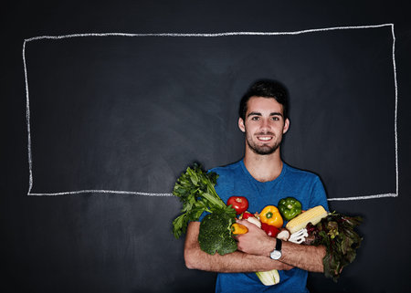 Healthy starts with me. Studio portrait of a young man carrying vegetables against a chalk...