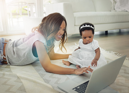 A mother using a laptop with and her baby daughter at home.の写真素材