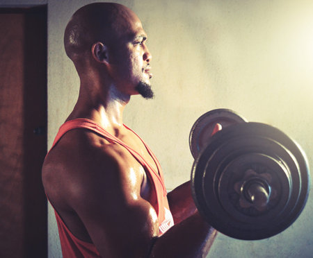 Building his body one rep at a time. a muscular young man lifting weights.