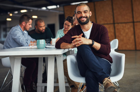 The creative process. Portrait of a young man sitting at a table in an office with colleagues...