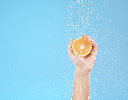 Hand, orange and water with natural skincare for health, wellness and organic fruit on a blue studio background. Beauty, fresh and food for juicy vitamin c skin care treatment for dermatologyの写真素材