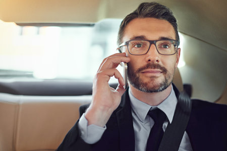 Doing business while on the move. a businessman using his cellphone while sitting in the backseat of a car.の写真素材