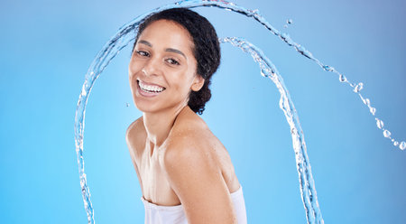 Beauty, splash and black woman in studio portrait for cleaning body or skincare promotion with water on blue mockup. Face, skin care model with water drops or shower in bathroom for morning facialの写真素材
