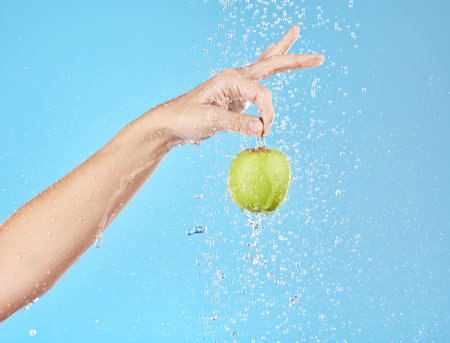Apple, water and hand with fruit hanging for vitamin healthcare or nutrition sustainability in studio. Healthy body wellness, detox health and healthy food under water in blue studio backgroundの写真素材