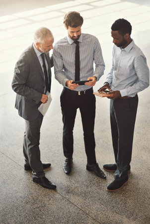 Meeting on the move. High angle shot of businesspeople standing in a office lobby.の写真素材