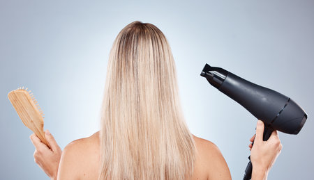 Hair care, back and woman with a product for styling, drying and brushing against a grey studio background. Salon, beauty and model with a hair dryer and brush for straight hair and hairstyleの写真素材