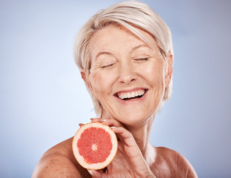 Grapefruit, skincare and senior woman excited about food for health of skin against a grey mockup studio background. Wellness, happy and elderly model with fruit for nutrition, diet and beautyの写真素材