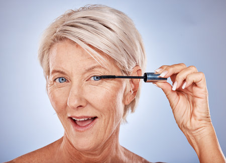 Makeup, mascara and portrait of a senior woman with a natural, cosmetic and beauty routine in a studio. Cosmetics, beautiful and elderly model with a eyelash product isolated by a gray background.の写真素材