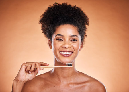 Dental care, toothbrush and hygiene with a model black woman brushing her teeth in studio on a beige background. Portrait, face and oral treatment with an attractive young female proud of her routineの写真素材