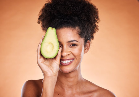 Beauty, skincare and avocado with a model black woman in studio on a beige background for wellness or antioxidants. Portrait, skin or nutrition with an attractive young female proud of healthy eatingの写真素材