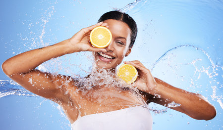 Water splash, lemon and skincare with beauty, product and advertising body wellness, cleaning and hygiene in blue studio background. Health, clean or skin with an young female model and natural fruitの写真素材