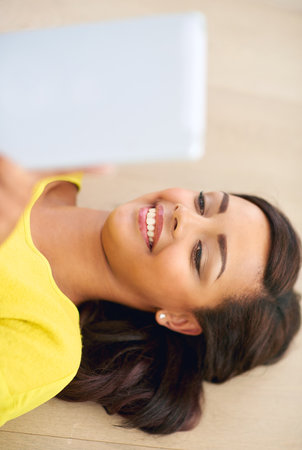 Checking in with her friends online. a young woman using a digital tablet at home.の写真素材