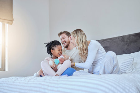 Interracial, adoption family and bed with smile, happiness and bonding together with kid, home and love. Diversity, happy family and sitting in bedroom with child, african girl and parents in houseの写真素材