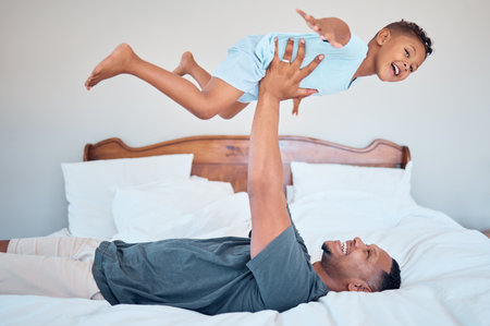 Happy, airplane and father with child in bedroom for relax, support and bonding together. Smile, balance and games with dad playing with son in family home for freedom, funny and affectionateの写真素材