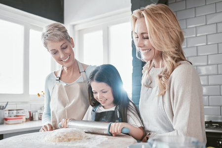 Baking, bonding and child with mother and grandmother in the kitchen learning to bake in their house. Food, love and girl kid with a smile with mom and senior woman teaching to cook togetherの写真素材