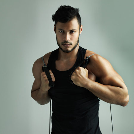 Training hard to be the best. Studio shot of a young man working out with a resistance band against a gray background.の写真素材