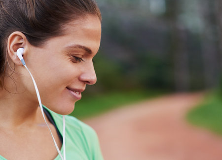 Music motivates her. a young woman listening to music while out running.の写真素材