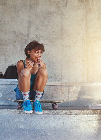 Time to recharge. a young woman sitting on her skateboard.の写真素材