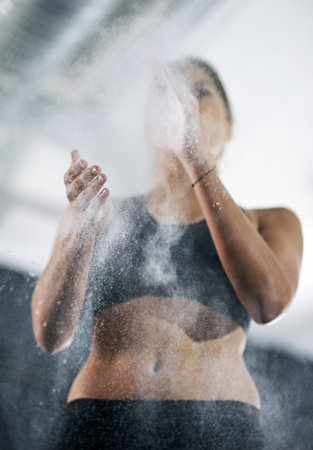 Let the weight training begin. a young woman coating her hands with sports chalk.