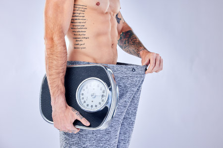 Motivation, health and weight loss, man with scale checking change from diet, workout and healthy lifestyle on studio background. Fitness, nutrition and wellness, balance in body care for male model.の写真素材