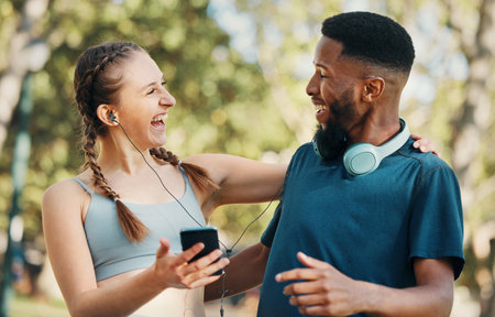 Headphones, fitness and couple with phone in nature on break after workout, running or training. Sports, diversity and man and woman streaming music, radio or podcast outdoors on 5g mobile smartphoneの写真素材