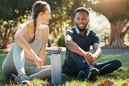 Couple, exercise and relax on grass in nature park for fitness rest, water hydration and interracial health discussion. Diversity, friends conversation and healthy cardio training break togetherの写真素材