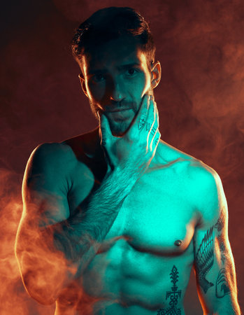Fitness, tattoo and man in studio for wellness, exercise and body goals with smoke, fire and danger aesthetic. Portrait, sexy and male model with misty atmosphere pose for training, muscle and powerの写真素材